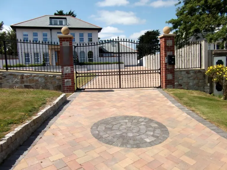 Black arched driveway gates and matching railings between brick pillars at a large house
