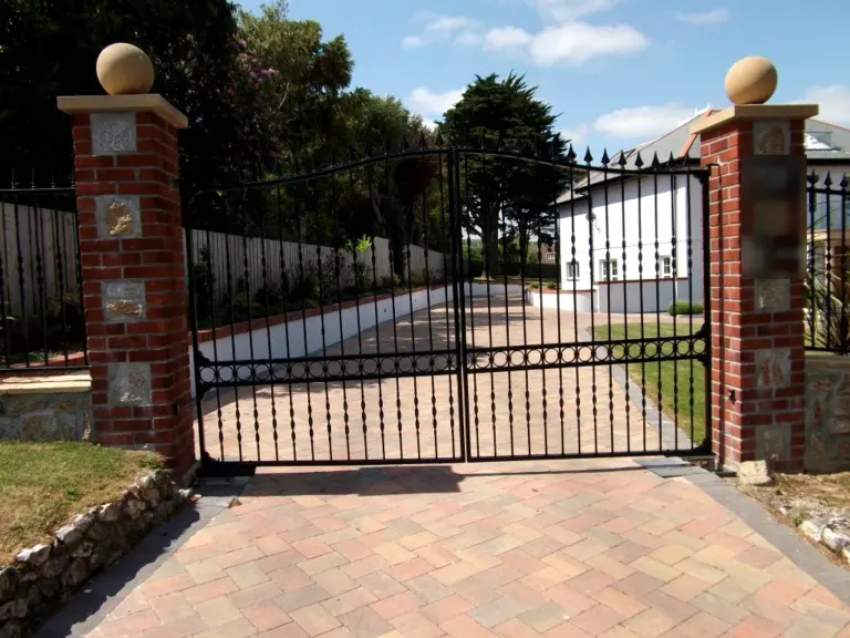 Pair of black arched driveway gates with spear tops and twisted bars between brick pillars