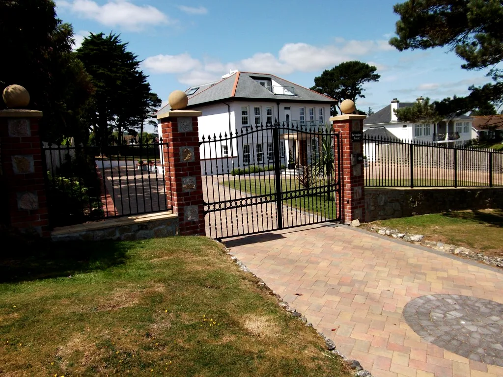 Black arched wrought-style driveway gates with matching railings at a white Cornish house