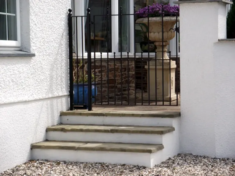 Black metal pedestrian gate with ball finials at the top of stone steps