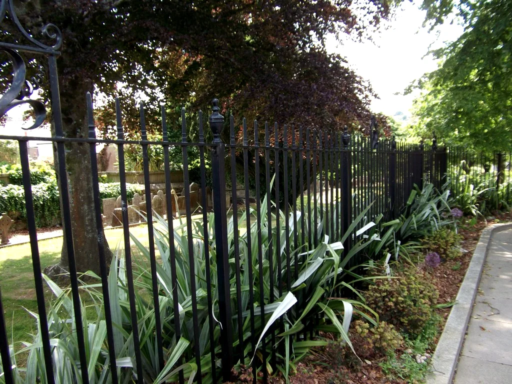 Black spear-top churchyard railings with urn-finial posts beside a paved path