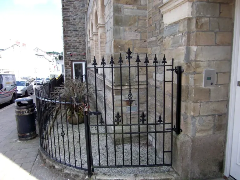 Black gate and curved railings with spear finials beside a stone town building