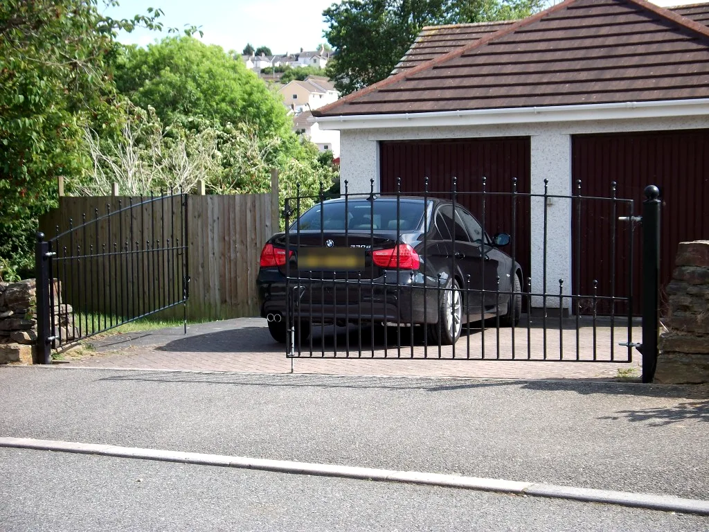 Black metal driveway gates with slim bars and ball-topped posts at a family home