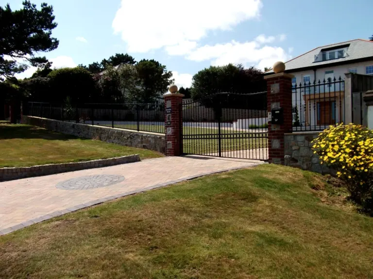 Long run of black estate railings and arched gates along a stone boundary wall