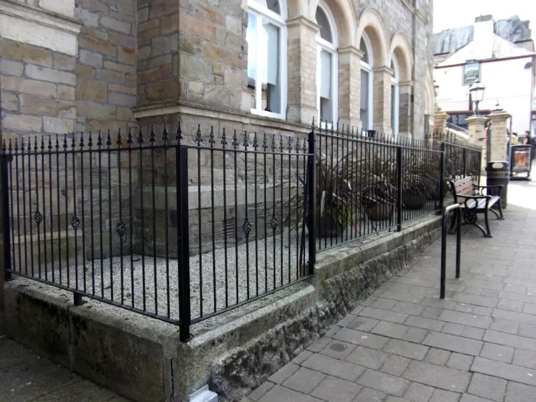 Black spear-top railings enclosing a planted gravel bed outside a historic stone building