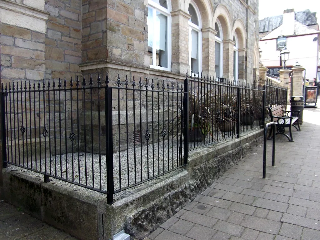 Black spear-top railings enclosing a planted gravel bed outside a historic stone building