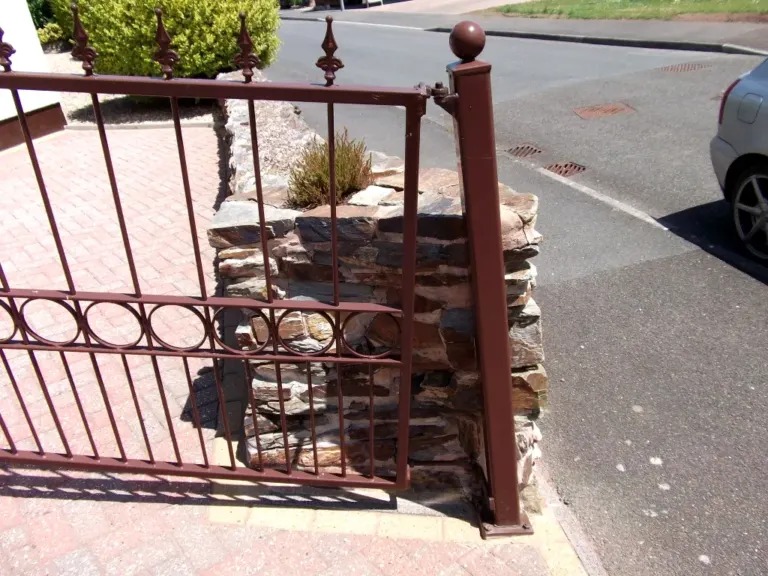 Detail of brown gate post with ball finial and hinge beside a slate stone pier