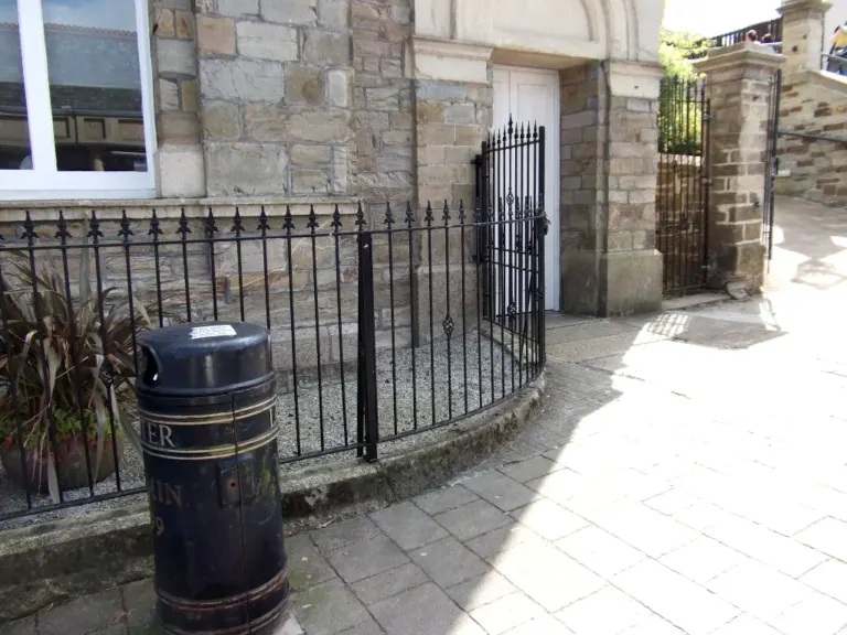 Curved black spear-top railings and matching gate beside a stone building doorway