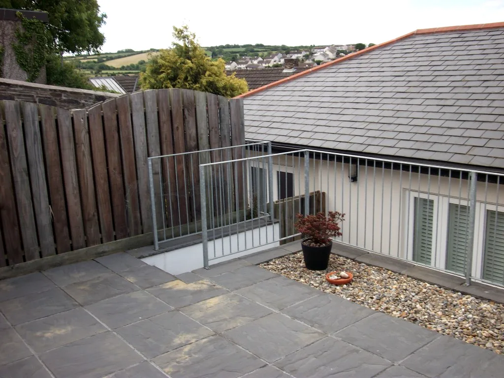 Galvanised guard railings around a slate patio with gravel border and potted acer