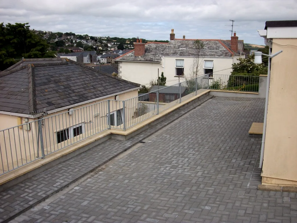 Galvanised flat-top guard railings edging a paved roof terrace above slate rooftops