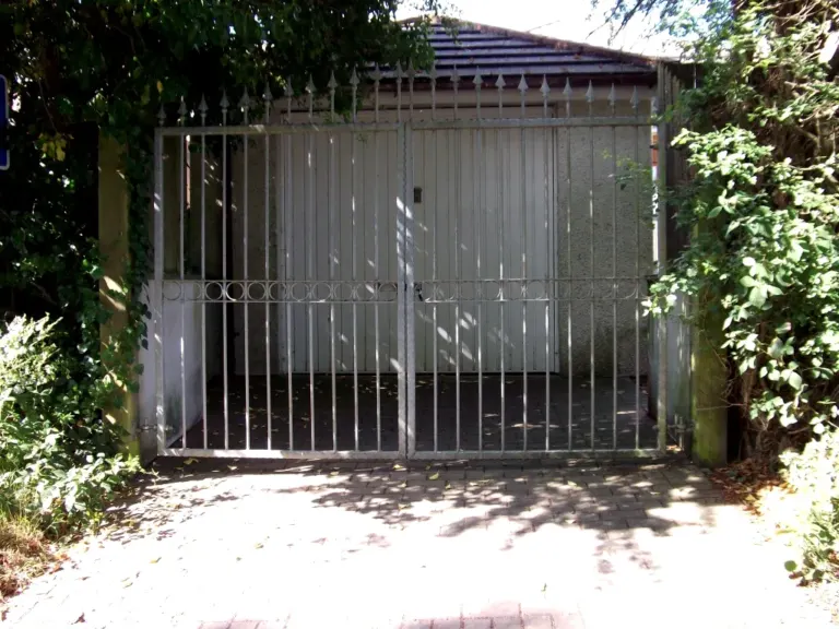 Pair of pale grey metal gates with spear tops and ring band before a garage