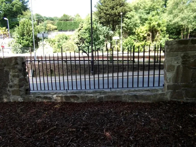 Black railing panel with scroll feature fitted between stone piers on a low wall