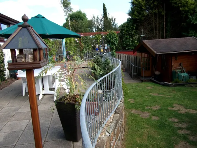 Serpentine galvanised railing following a curved stone wall around a raised garden patio