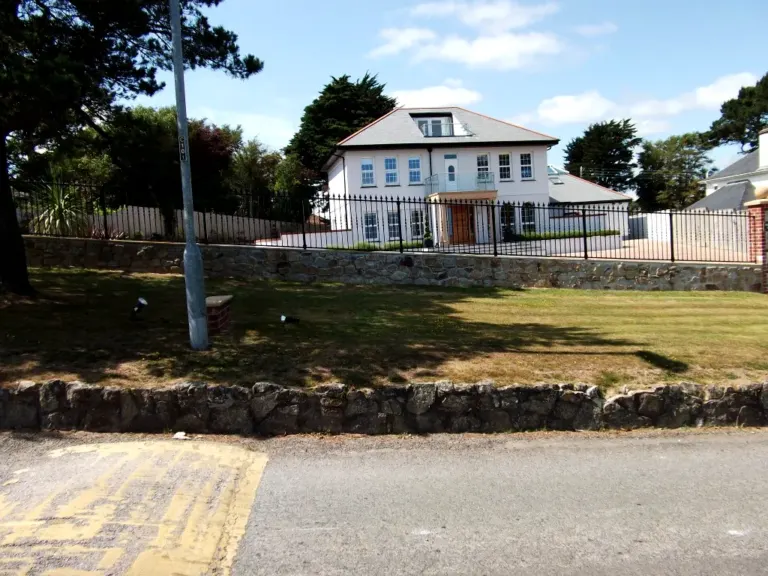 Long run of black spear-top railings on a stone wall fronting a large white house