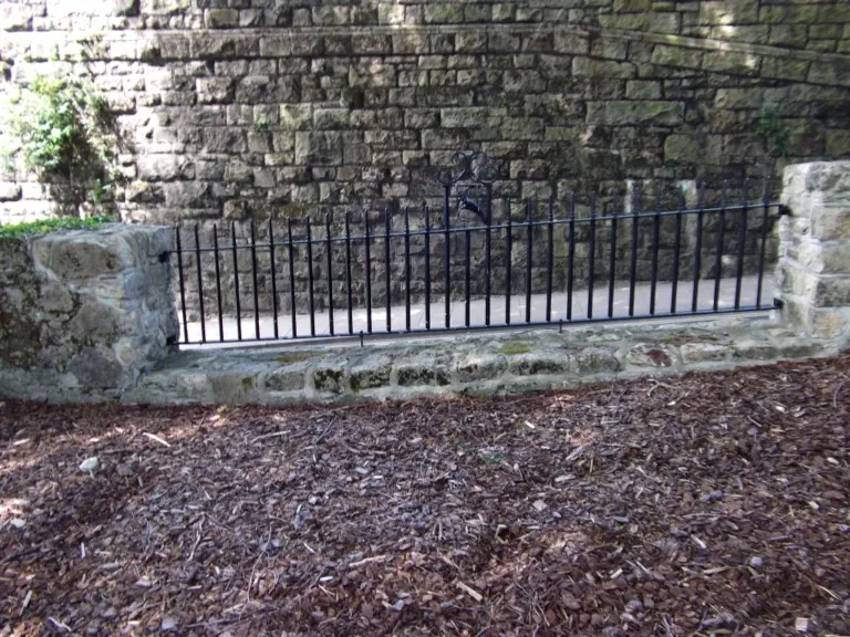 Black spear-top railing panel with scroll top between old stone piers
