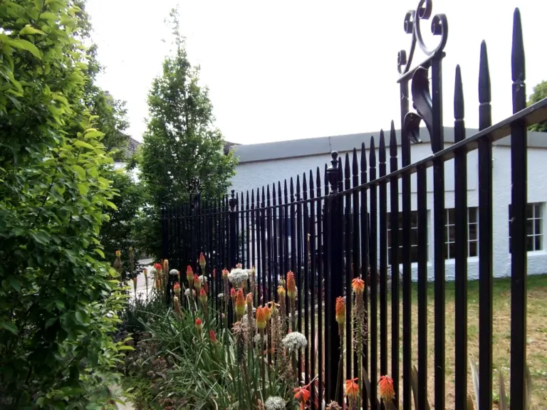 Black spear-top railings with scroll-topped post behind a border of red hot pokers