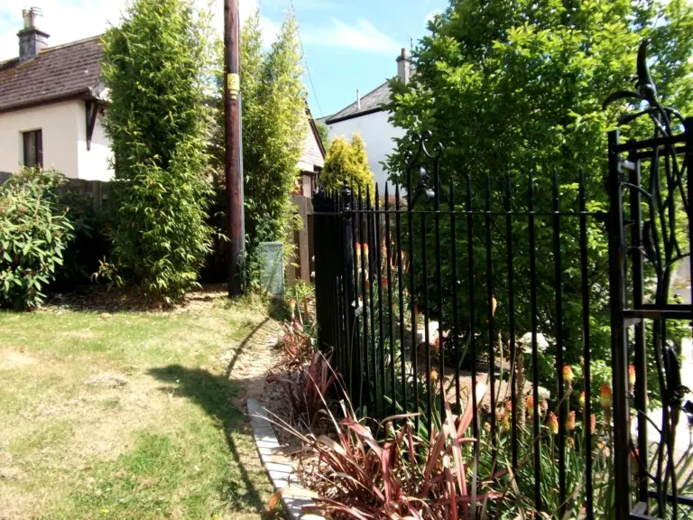 Black spear-top railings with scroll detail and ornate gate edge behind a planted border