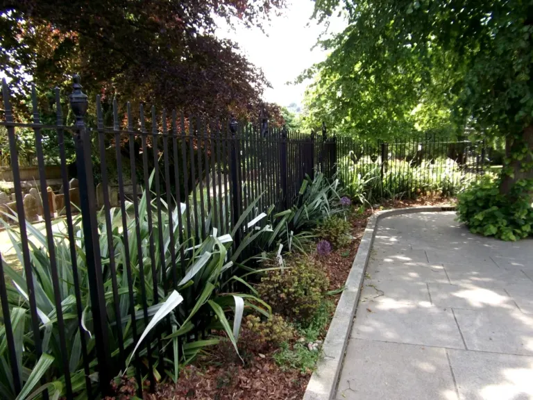 Traditional black railings with urn finials following a curving path beside a churchyard