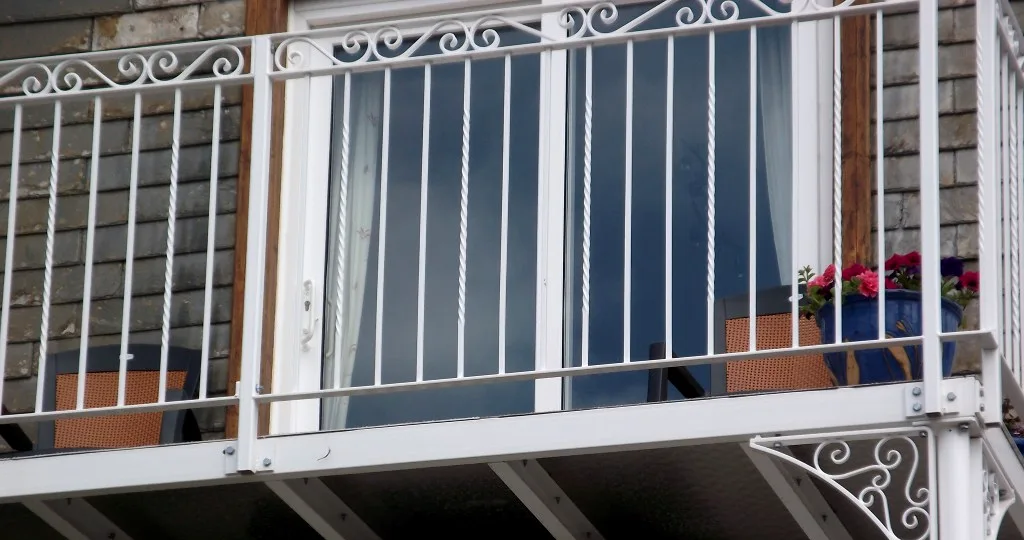 Close view of white balcony railings with twisted bars, scrolled frieze and potted red flowers
